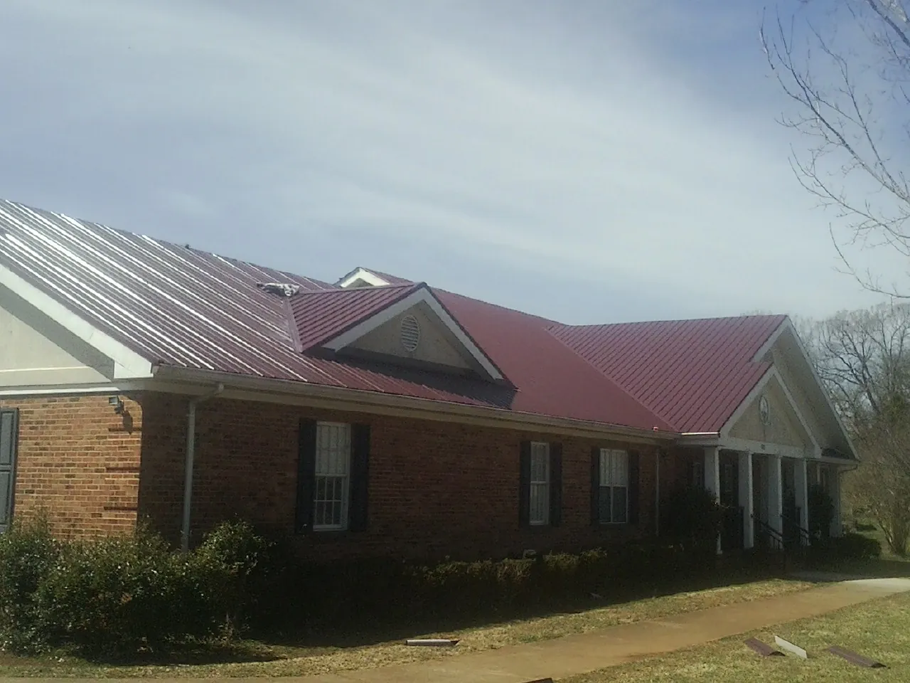 Red metal roof with gabled entries on a long brick building, from a Hail Damage Roof Repair job in Lisbon